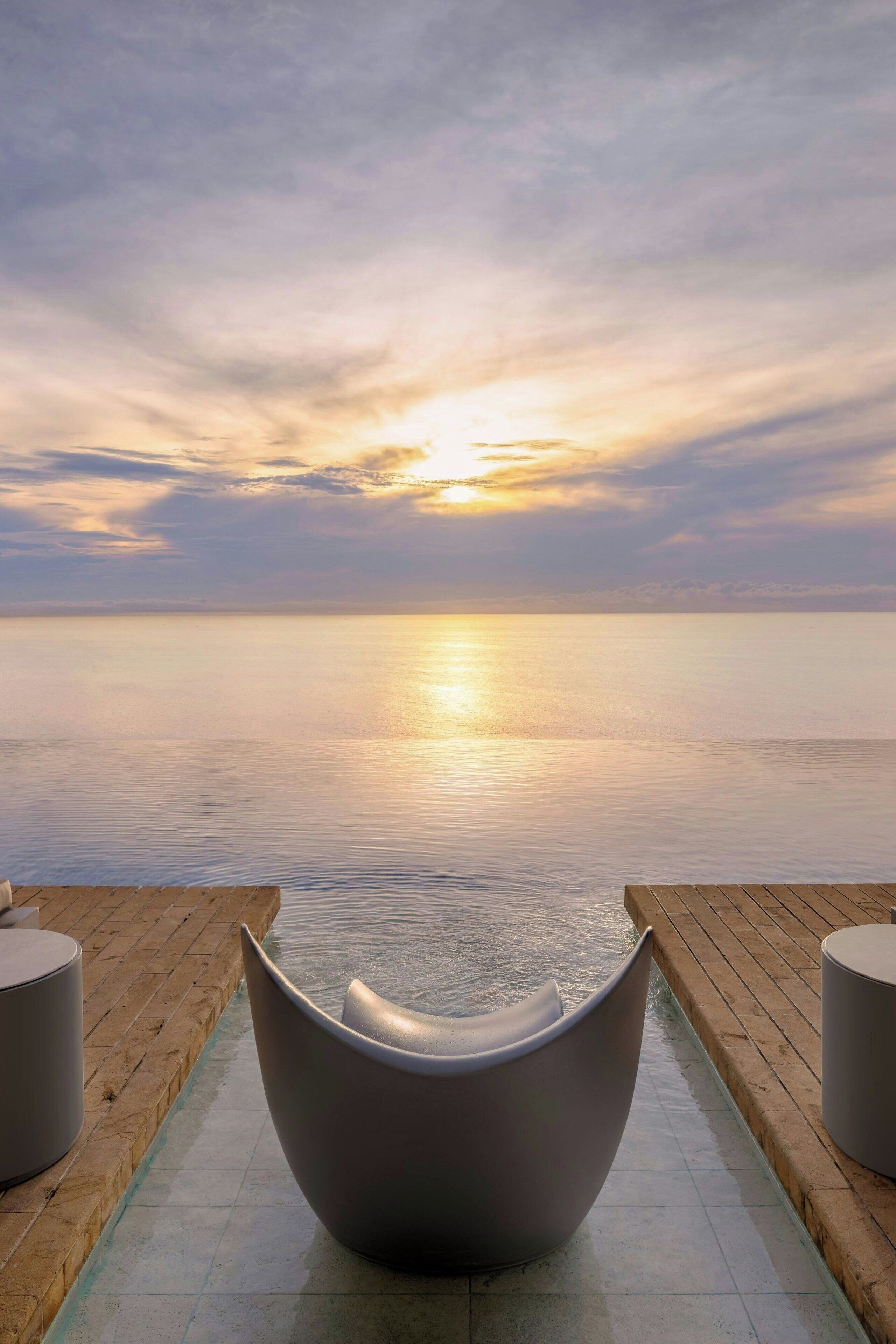 A serene outdoor seating area with a view of the sunset over the water.