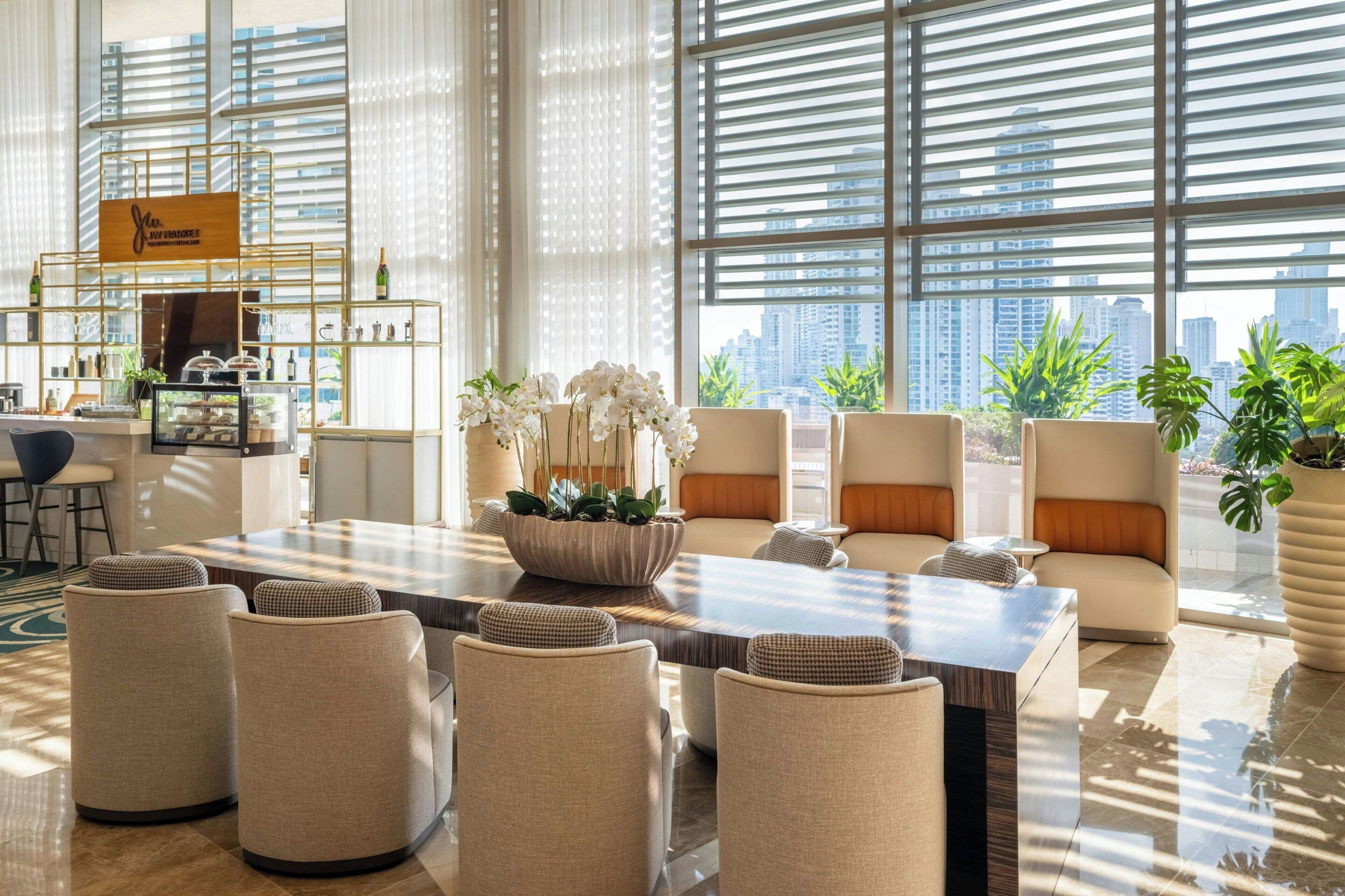 Un hall d’hôtel spacieux avec un espace salon central, un bar et une vue sur le paysage urbain grâce à de grandes fenêtres.
