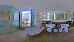 Een moderne badkamer met een groot bad, twee wastafels en een douchecabine met glazen wanden en uitzicht op de stad.
