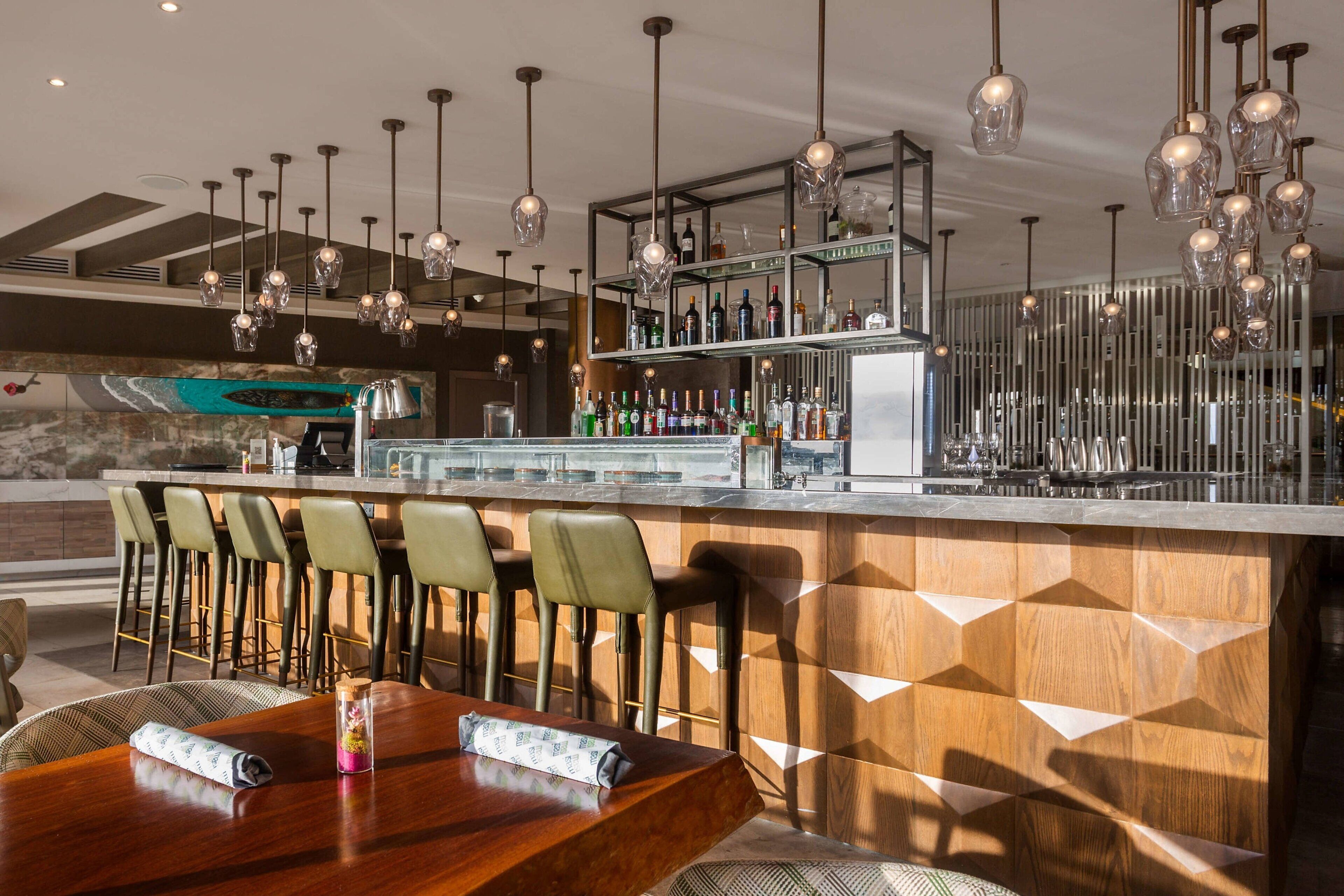 Un espace bar doté d’un comptoir en bois, de tabourets de bar et de luminaires suspendus.