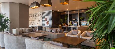A spacious lobby with modern furniture, pendant lighting, and a view of the bar area.