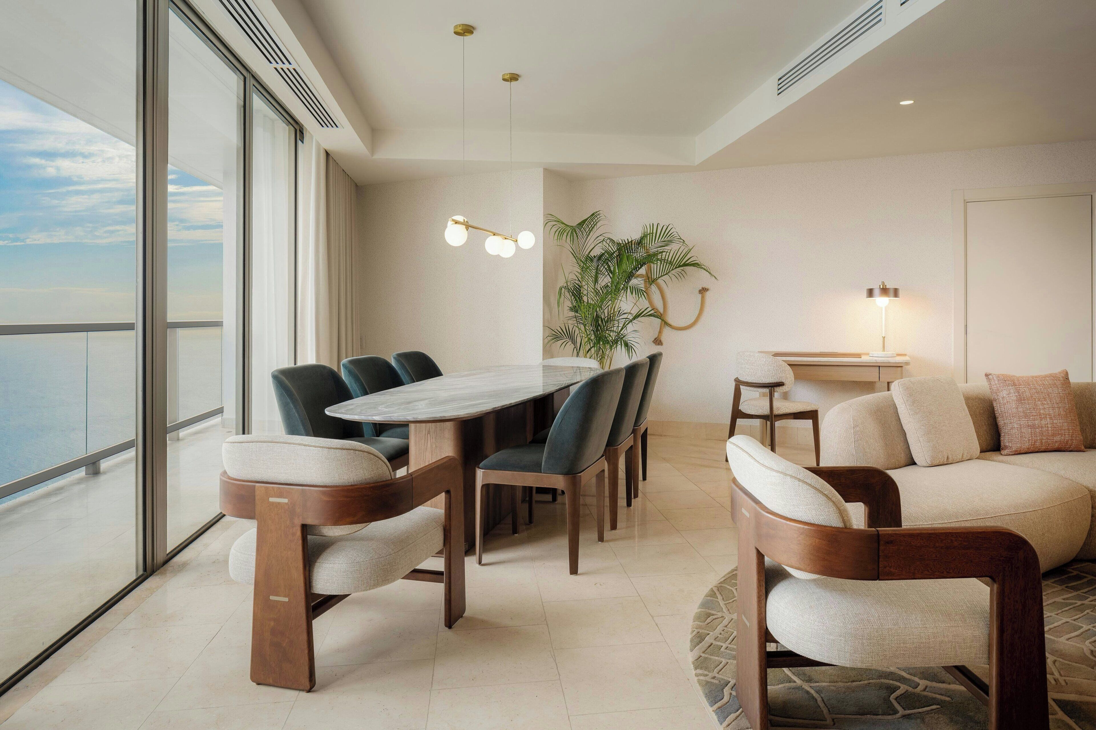 A modern dining area with a wooden table and chairs, a potted plant, and a sofa with cushions.