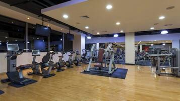 A gym with various exercise equipment, including treadmills and weight machines, arranged on a wooden floor.
