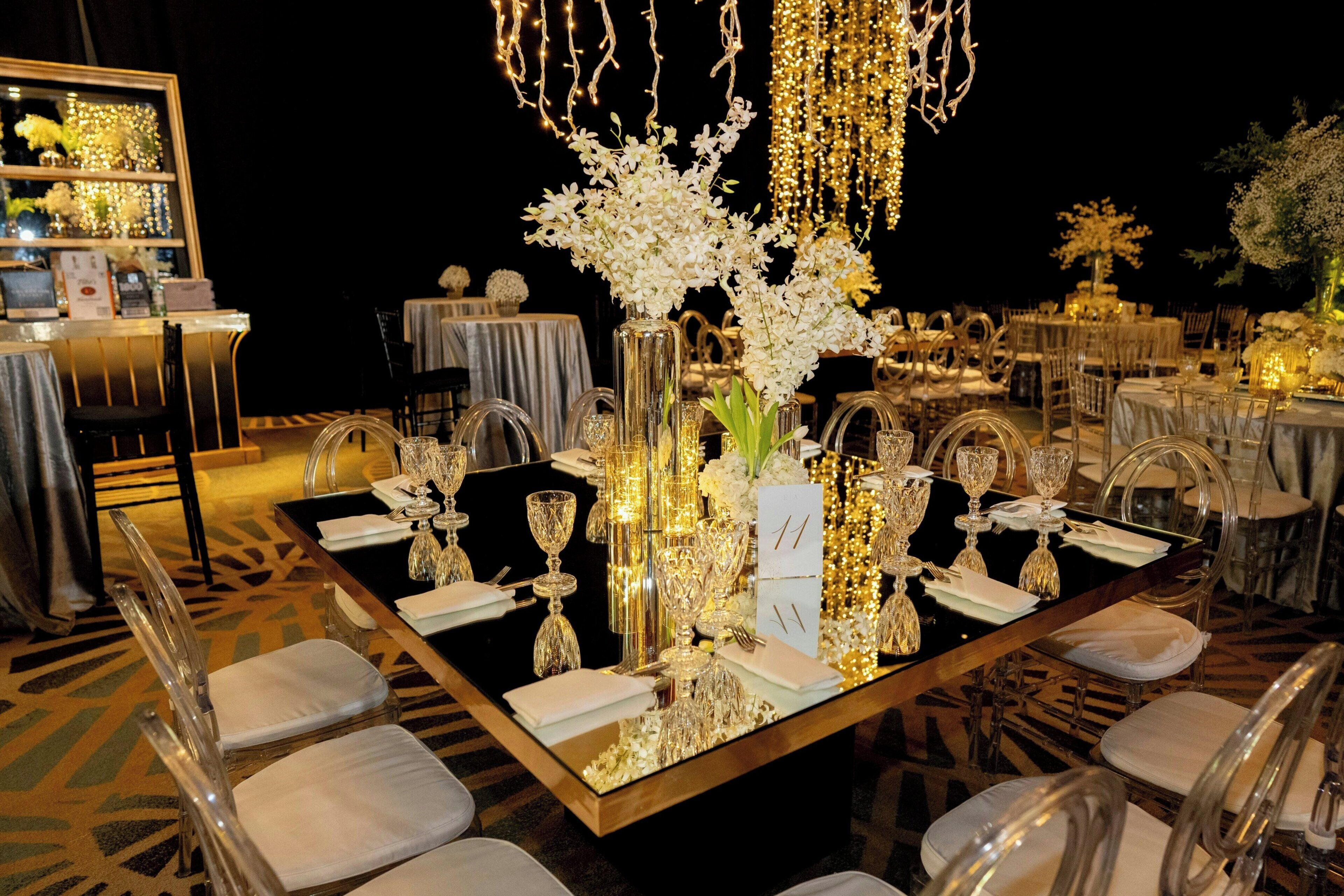 A banquet table set with clear glassware, white flowers, and a number sign.
