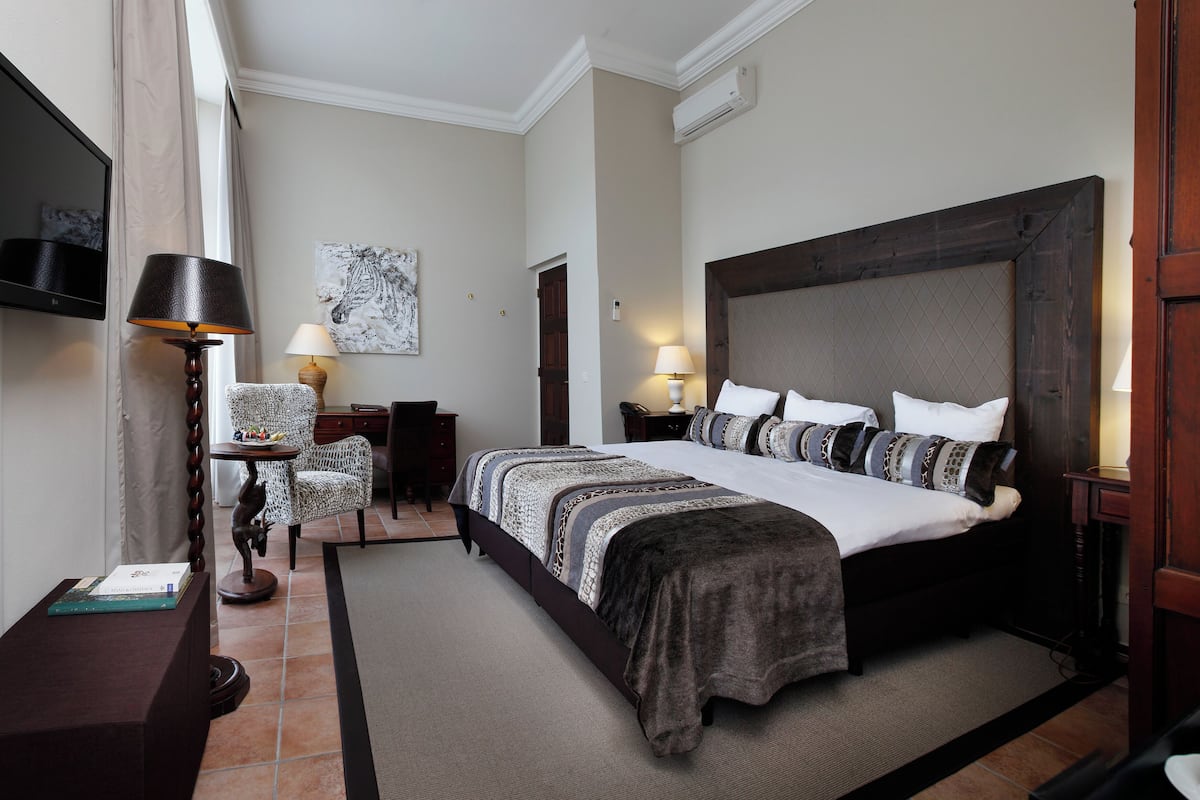 Habitación de hotel con una cama grande, un escritorio, una silla, un televisor y un cuadro en la pared.