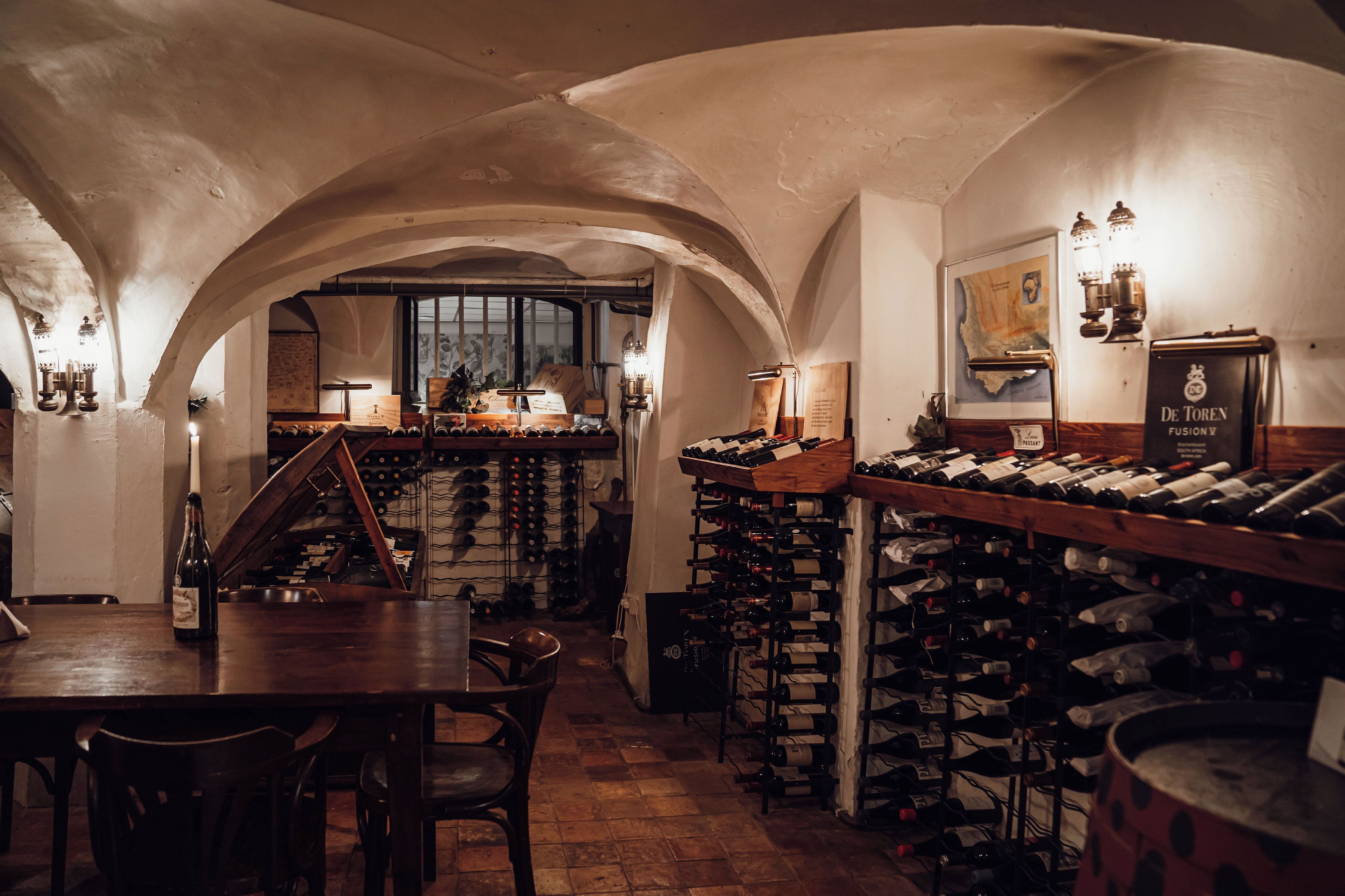 A wine cellar with wooden racks of wine bottles, a wooden table, and chairs.