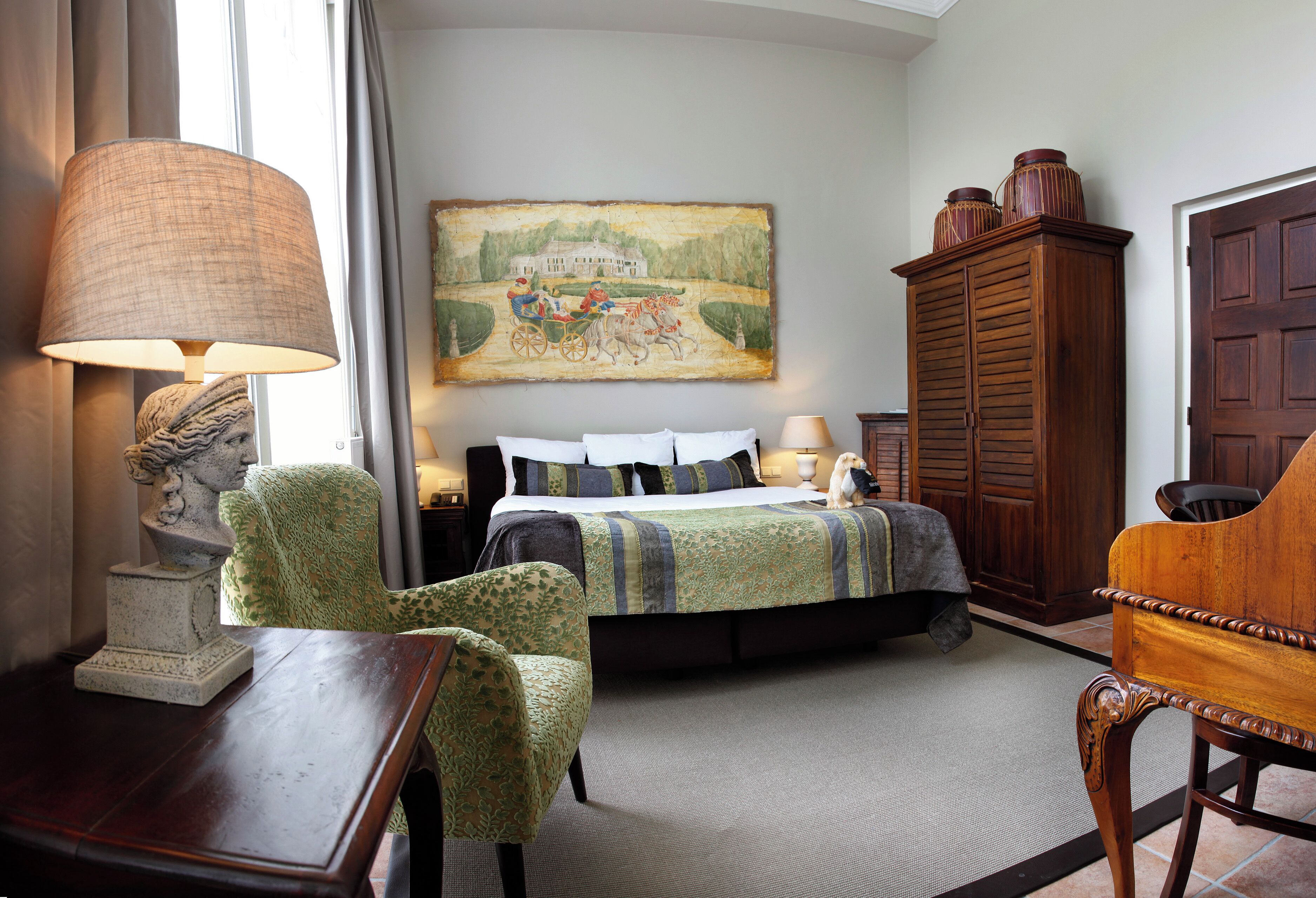 A bedroom with a bed, a green armchair, a wooden cabinet, and a painting on the wall.