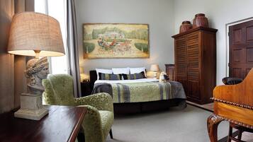 A bedroom with a bed, a green armchair, a wooden cabinet, and a painting on the wall.