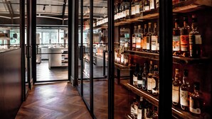Zona de bar con estantes llenos de botellas de licor y una cocina al fondo.