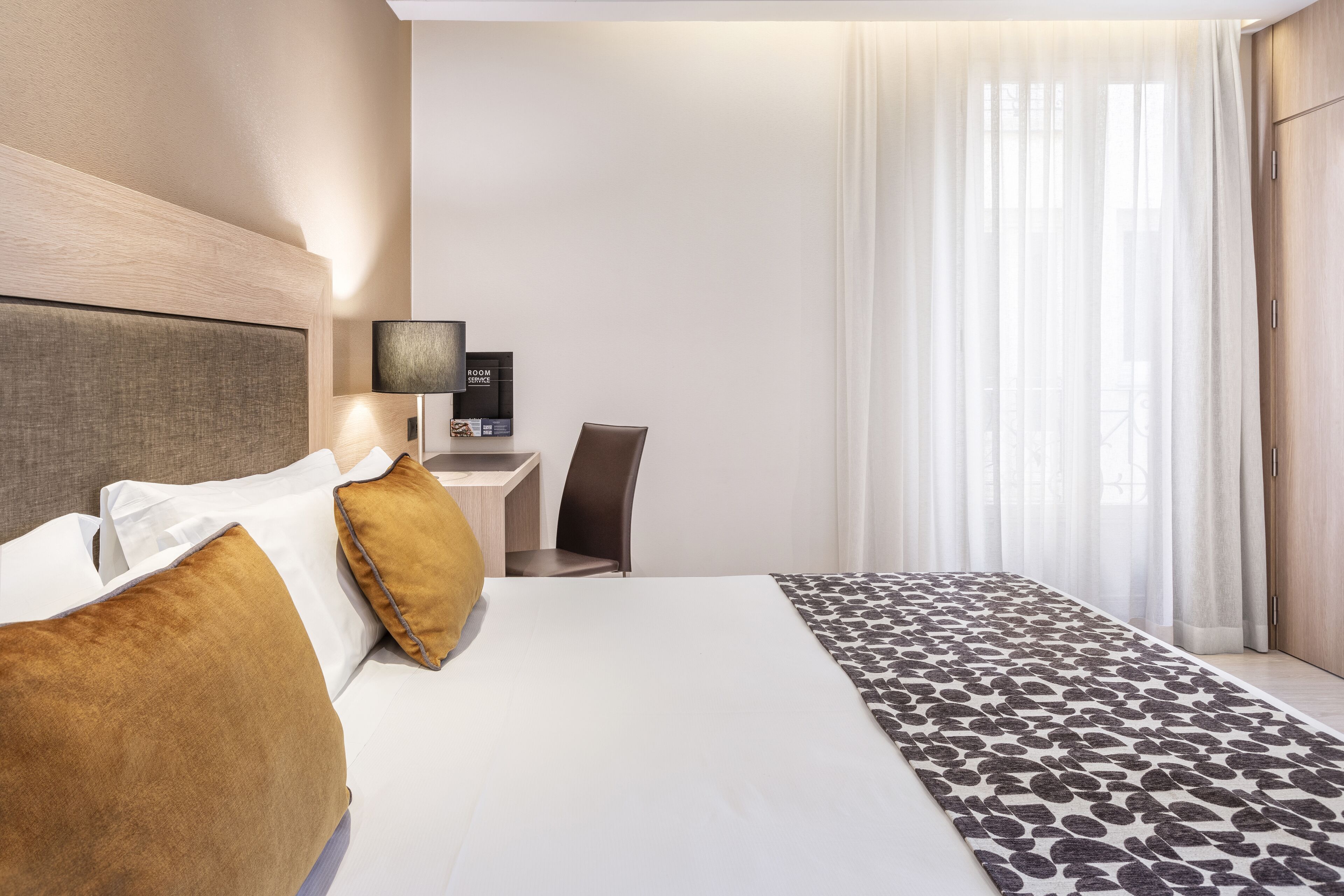 Ein Hotelzimmer mit einem Bett, einem Schreibtisch, einem Stuhl und einem Vorhangfenster.