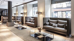A modern lobby with sofas, a glass coffee table, and a large pillar. - Catalonia Plaza Mayor (Madrid)