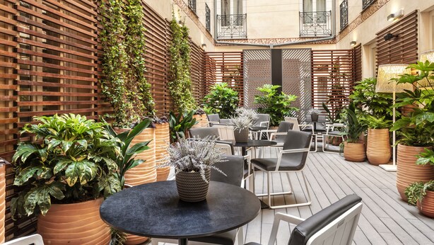 An outdoor patio area with round tables and chairs, surrounded by potted plants and wooden slats. - Catalonia Plaza Mayor (Madrid)