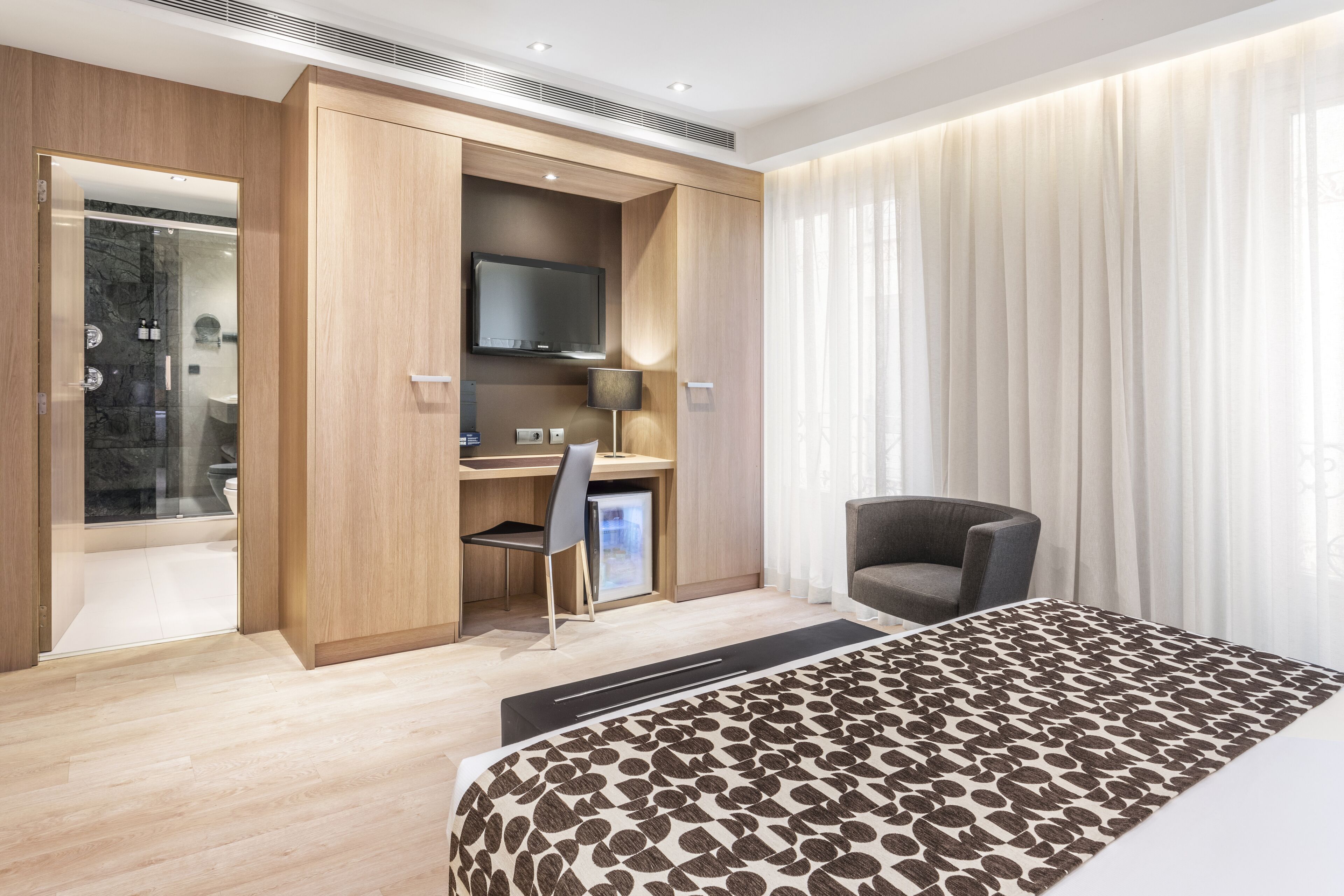 Een moderne hotelkamer met een bed, een bureau met stoel, een televisie en een douche.