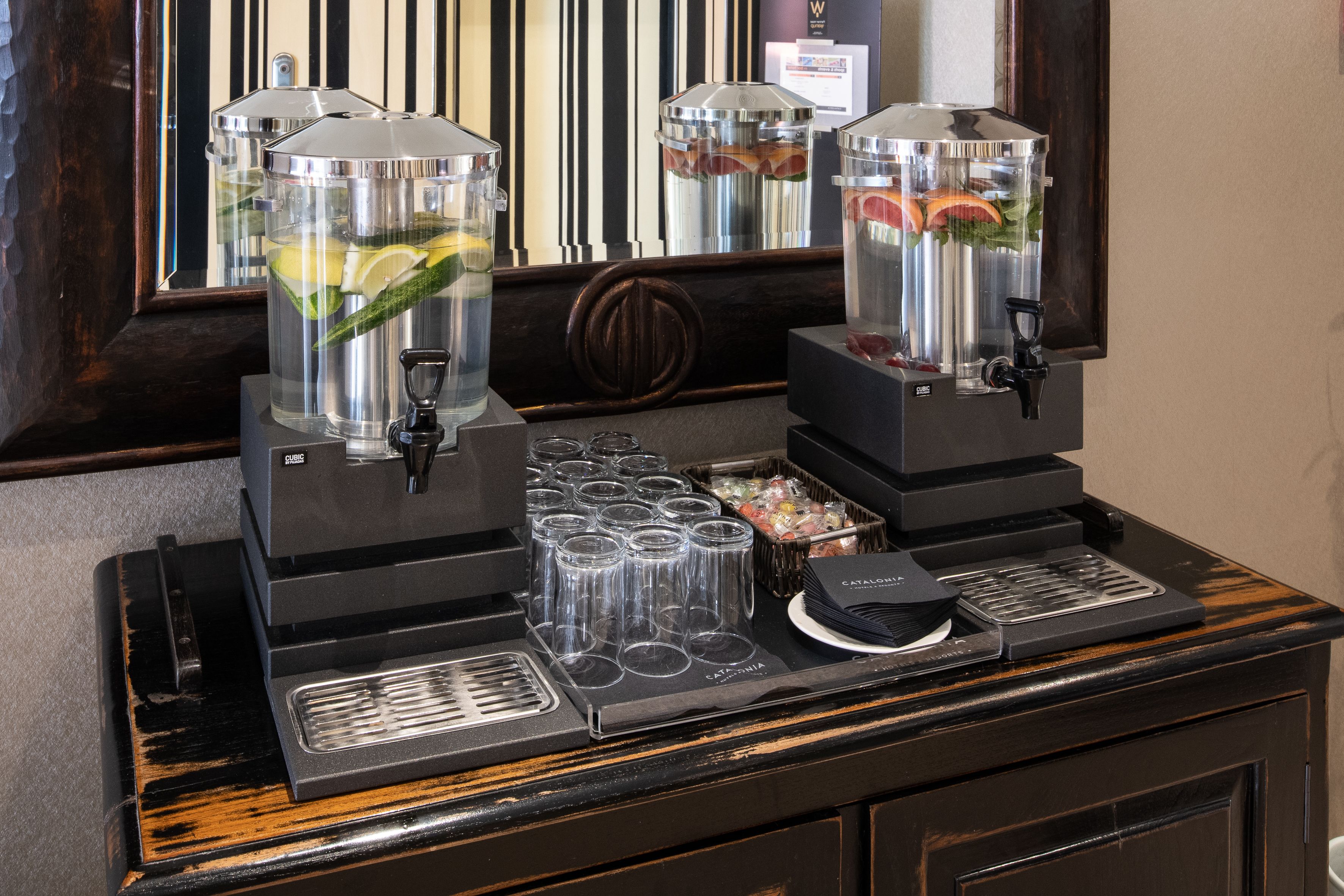 A coffee station with two coffee dispensers, a tray of cups, and a container of condiments.