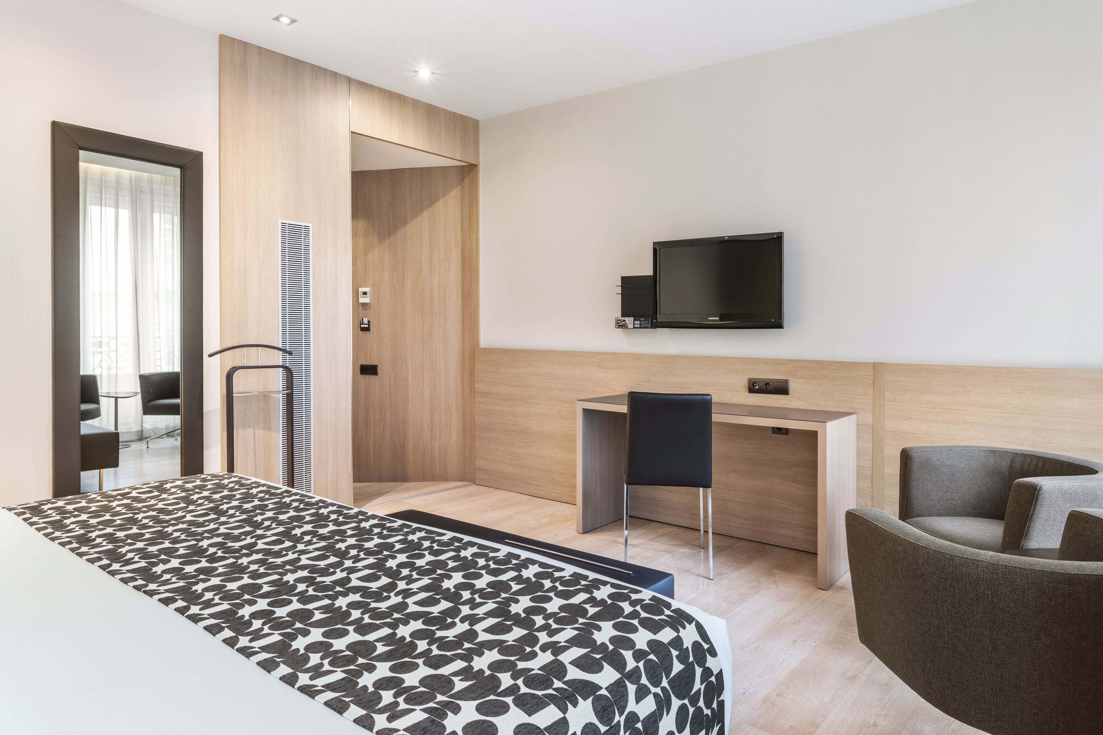 Una habitación de hotel moderna con una cama, un escritorio, una silla y un televisor en la pared.