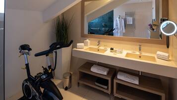 A modern bathroom with a dual sink vanity, a large mirror, and a stationary exercise bike.