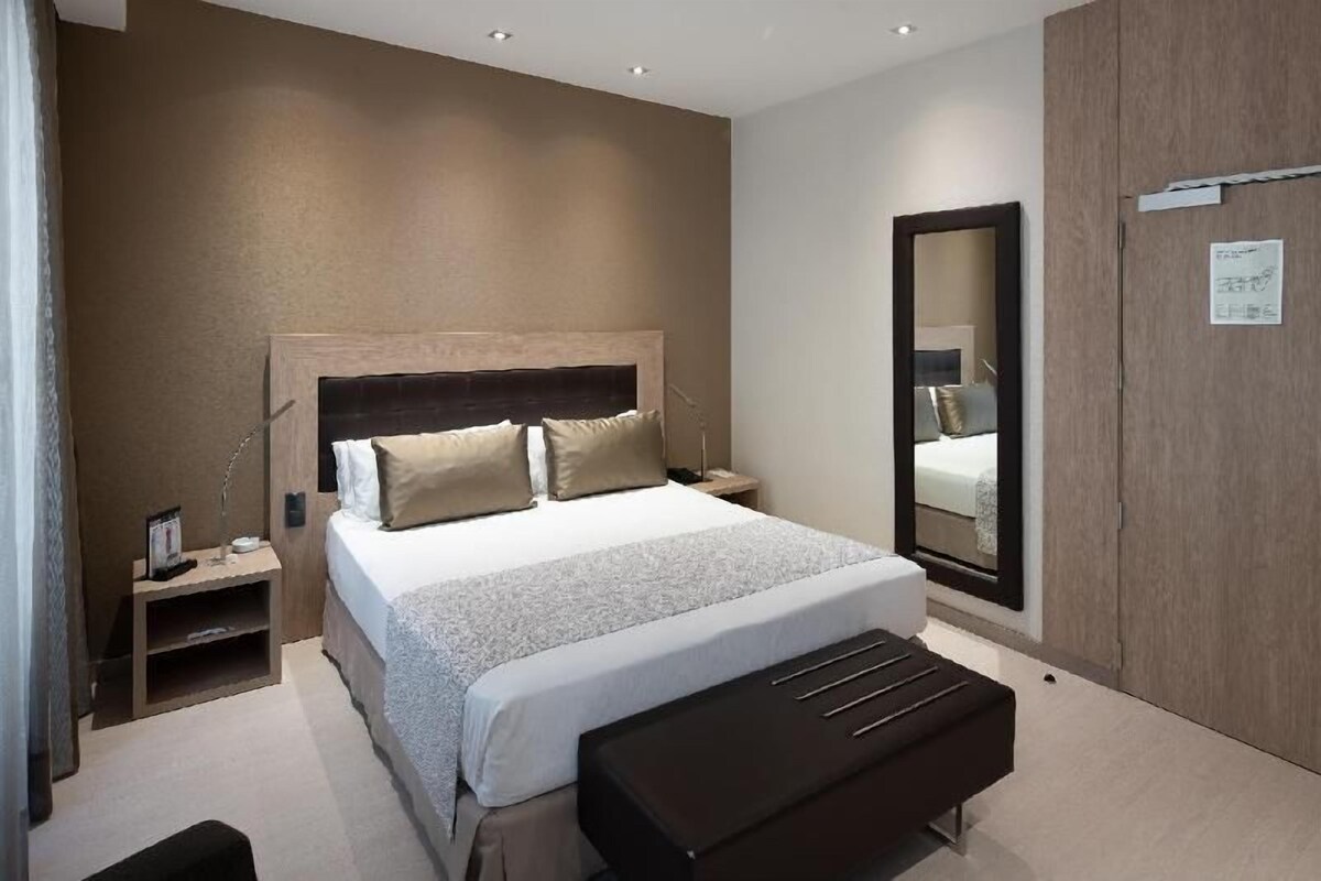 A bedroom with a bed, bedside tables, a bench, a mirror, and a wardrobe.