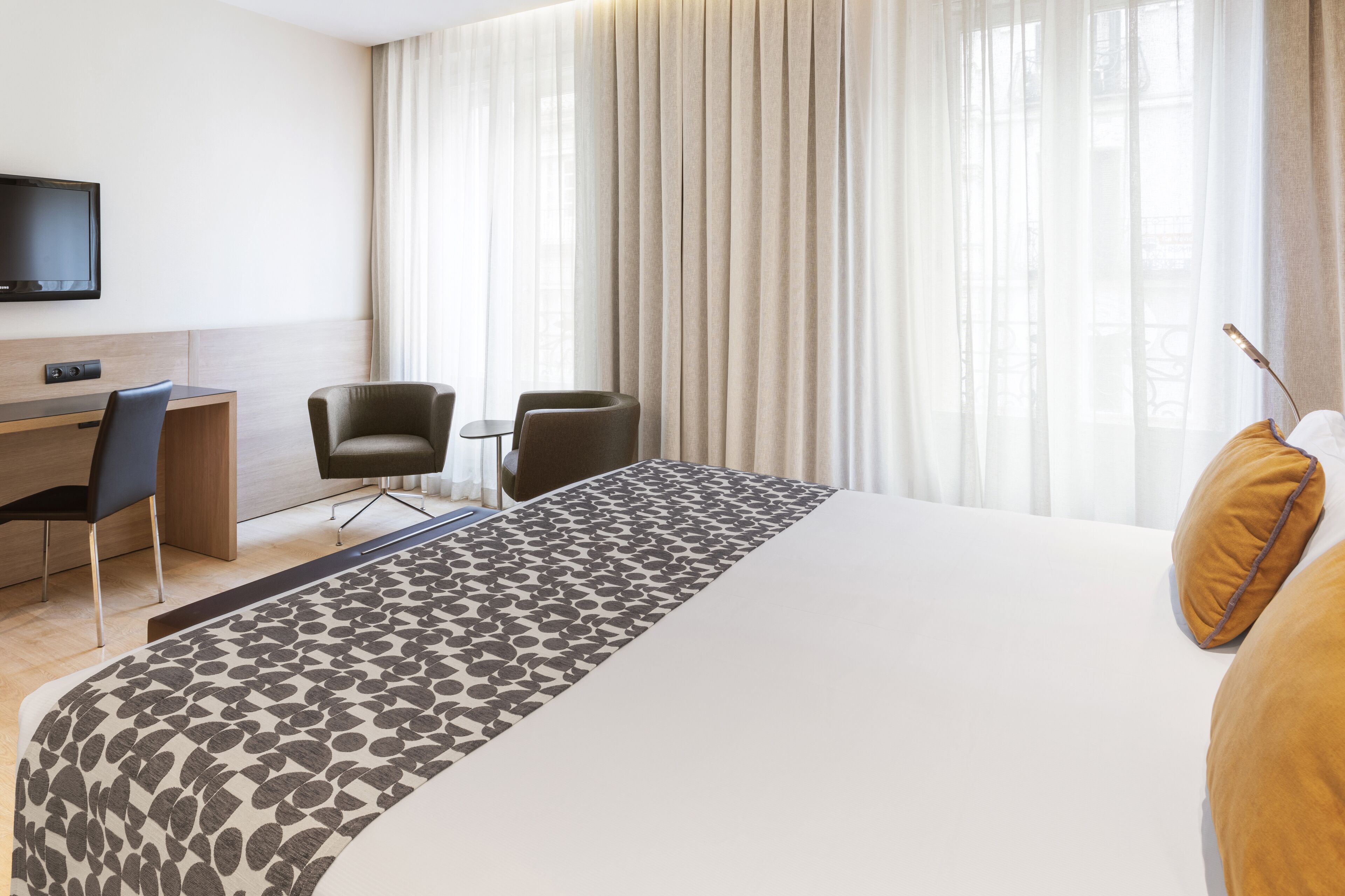 Una camera d'albergo con un letto grande, una scrivania con una sedia, una televisione e una finestra con tende.