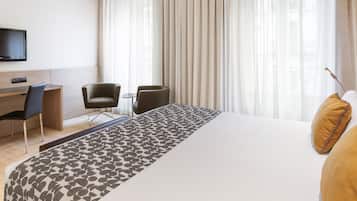 Ein Hotelzimmer mit einem großen Bett, einem Schreibtisch mit Stuhl, einem Fernseher und einem Fenster mit Vorhängen.