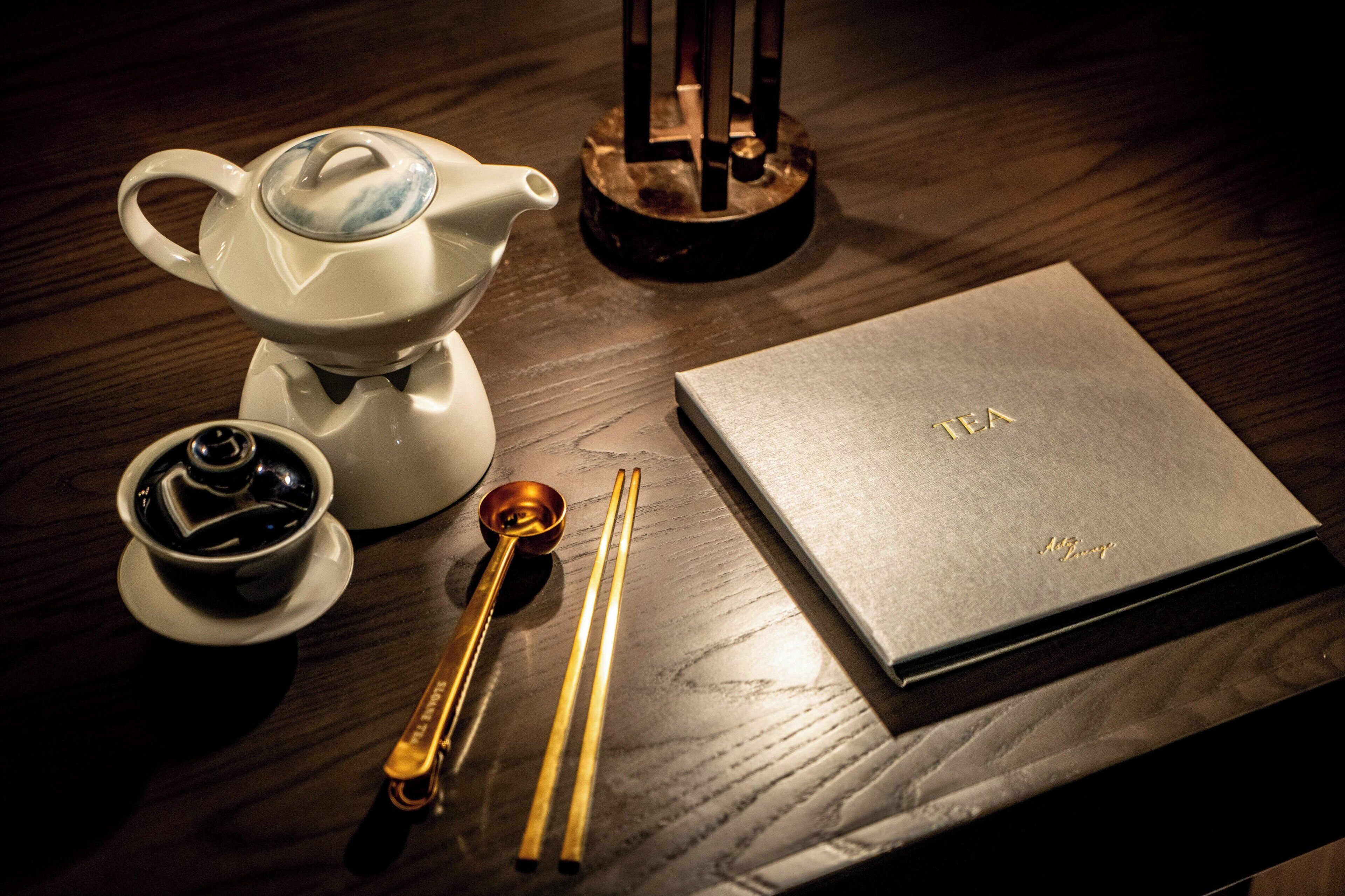 Una mesa con un calentador de té, una taza, un par de palillos y una caja de té.