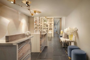 A modern reception area with a marble counter, a seating area with blue ottomans, and a shelving unit with books and decorative items.