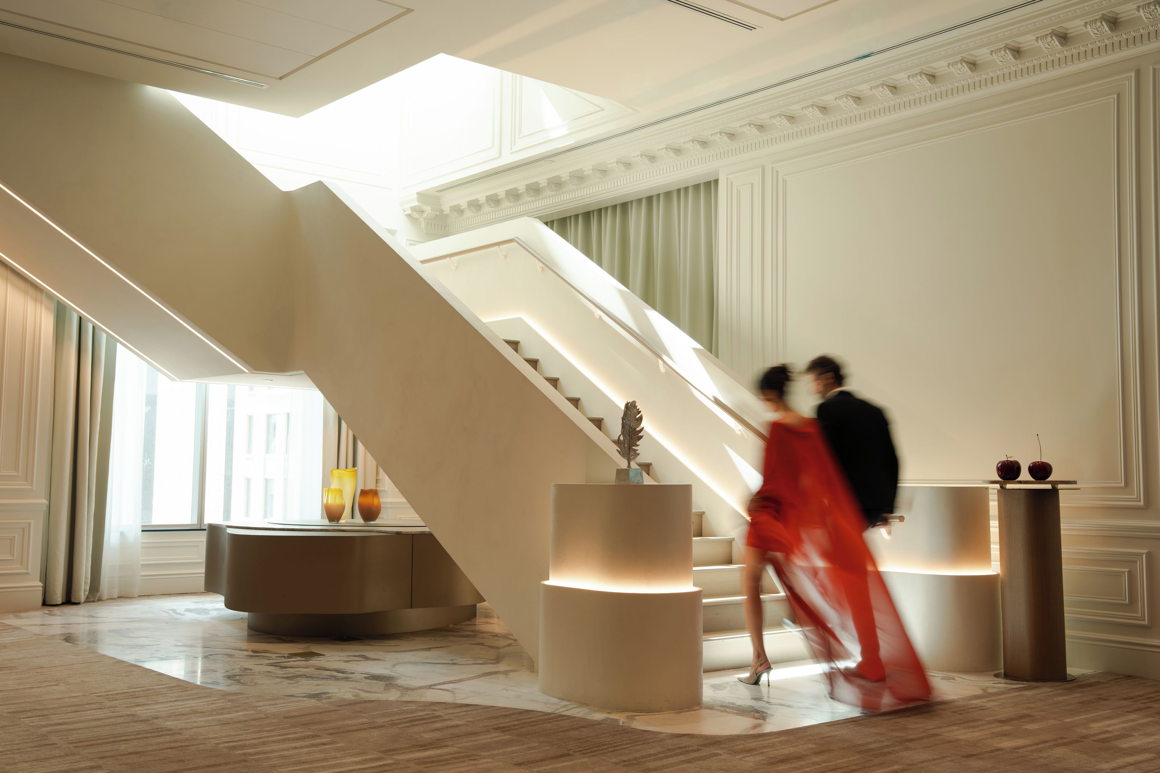A grand staircase with a modern design, a marble floor, and a decorative vase on a pedestal.