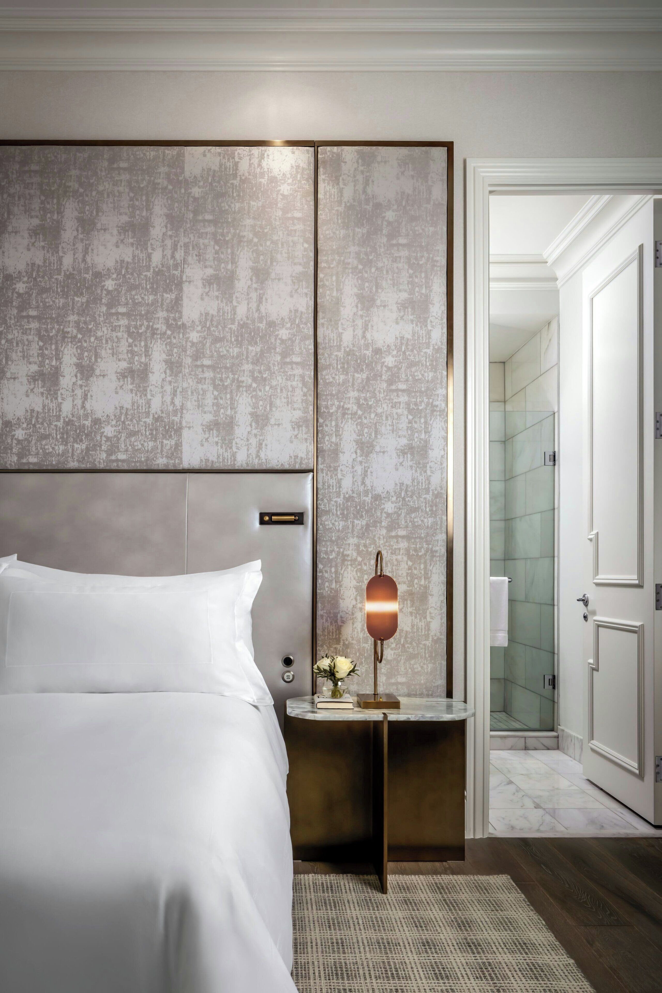Una habitación de hotel moderna con una cama grande, una mesita de noche con lámpara y vistas al baño.