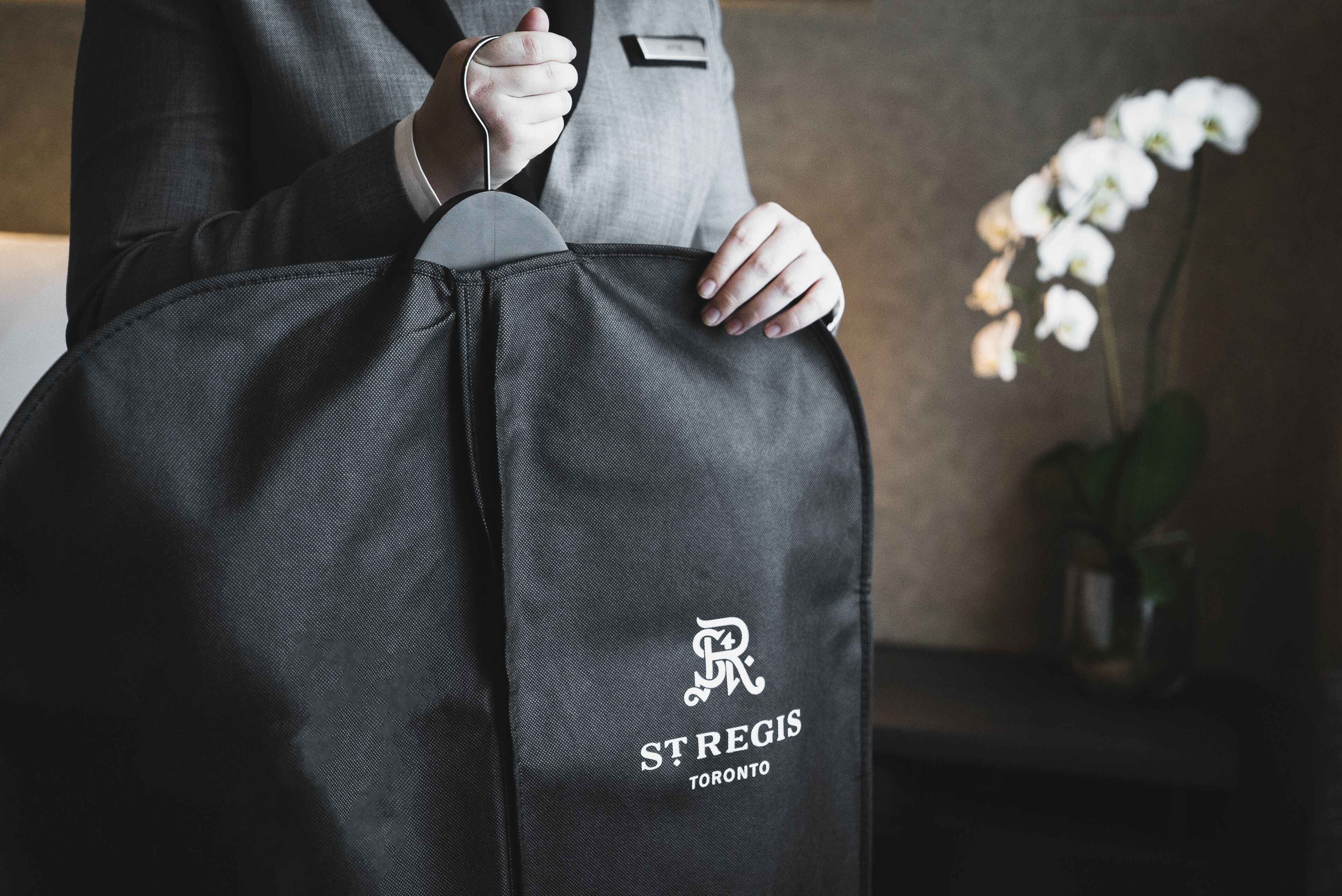 Een persoon die een zwarte tas vasthoudt met het logo 'St. Regis Toronto'.