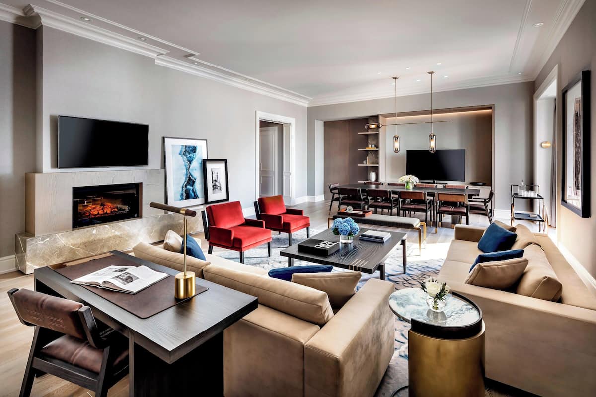 Un salon moderne avec un canapé, des fauteuils rouges, une table basse et un téléviseur fixé au-dessus d’une cheminée.
