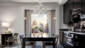 A modern dining area with a chandelier, a table with chairs, and a view of a cityscape through large windows.