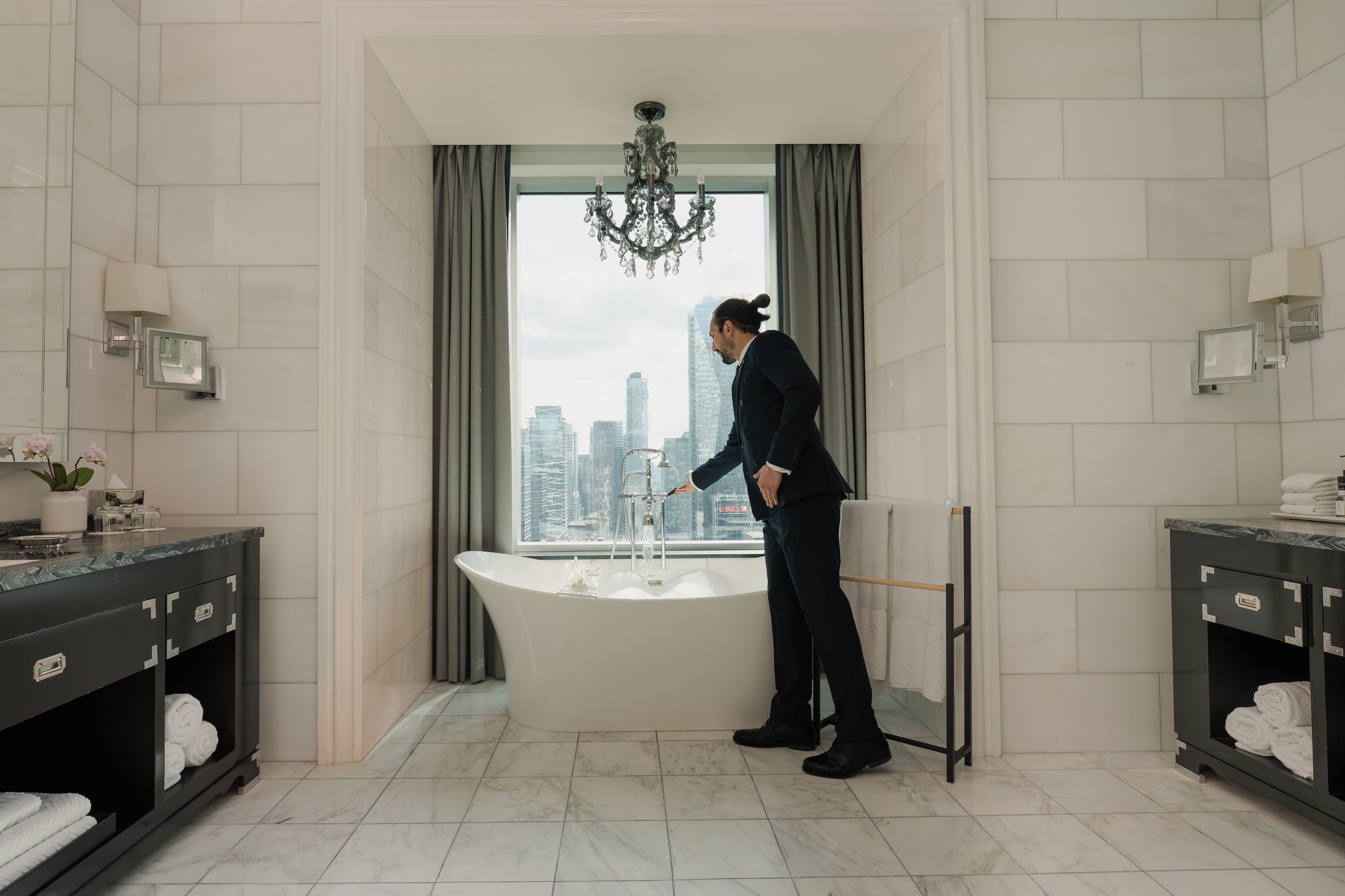 Un baño moderno con una bañera independiente, una araña y vistas a la ciudad.