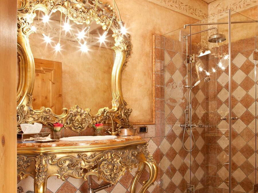 A bathroom with a large ornate gold mirror, a shower with a glass door, and a checkered tile floor.
