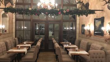 A restaurant with a chandelier, antler wall decor, and a long table with wine glasses and plates.
