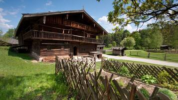A traditional wooden house with a balcony, surrounded by a wooden fence and a garden.