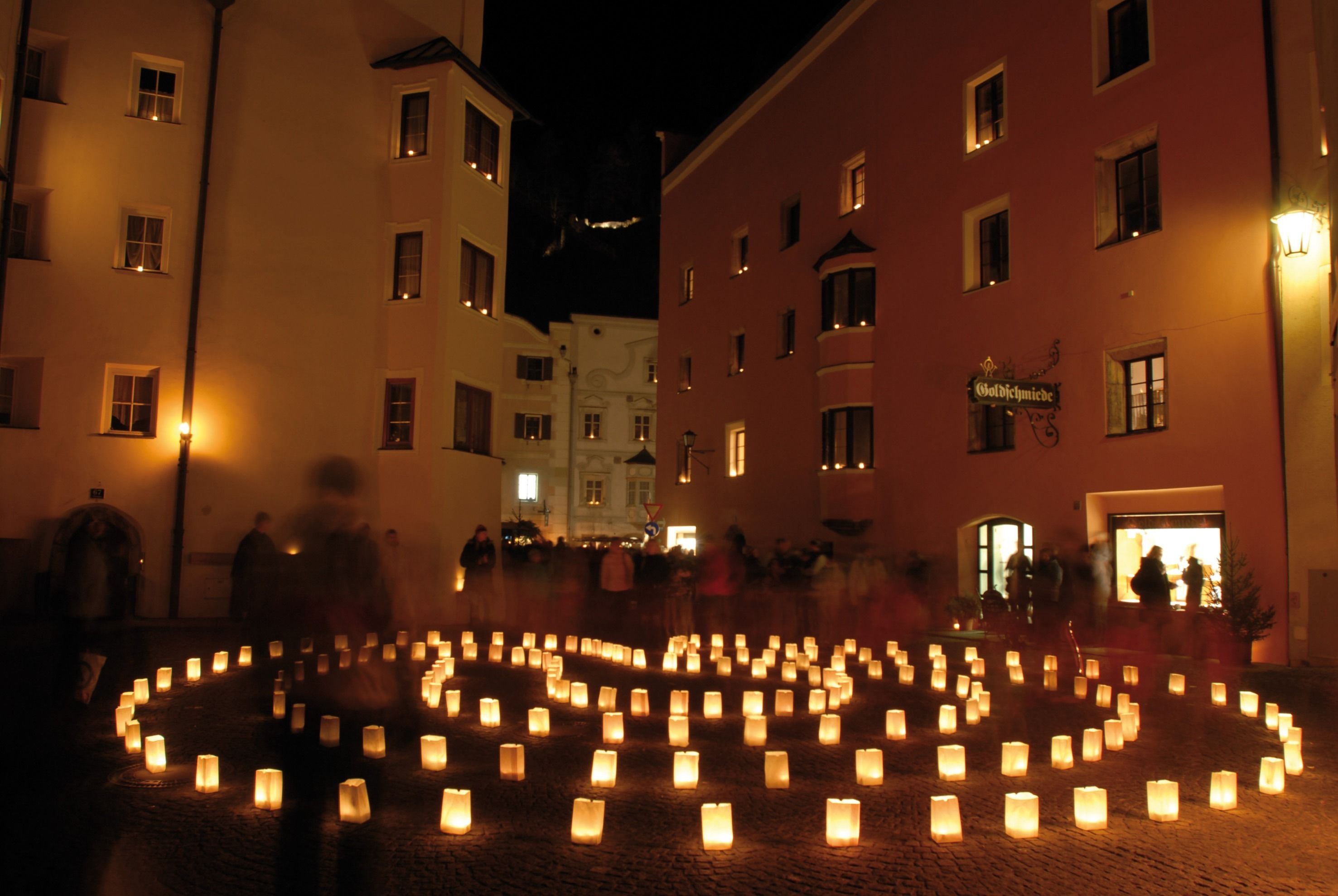 Un círculo de velas en una plaza adoquinada, rodeado de edificios con ventanas iluminadas.