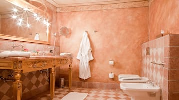 A bathroom with a vanity, sink, mirror, towel rack, toilet, bidet, and decorative lights.