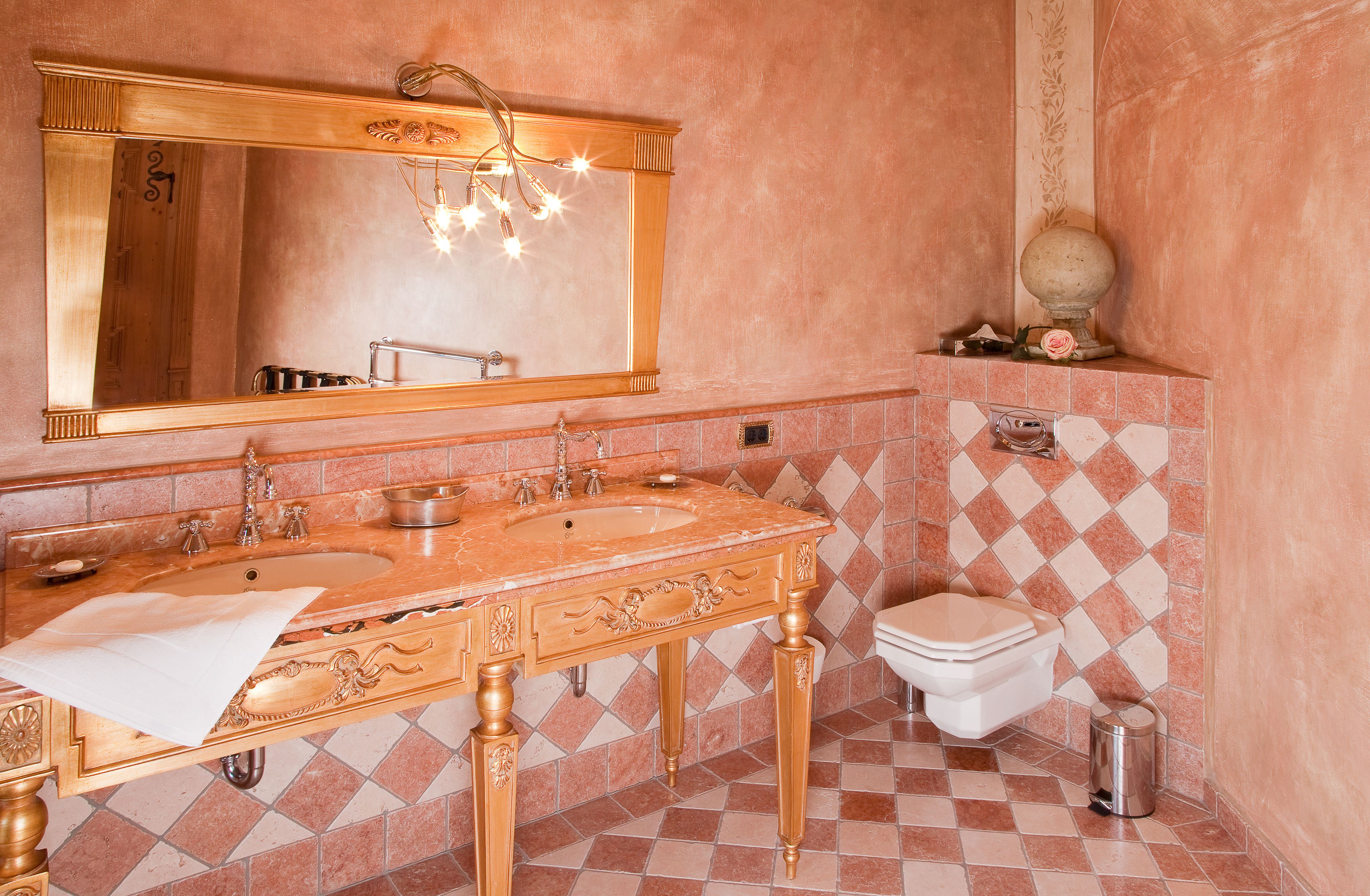 A bathroom with a large mirror, two sinks, a toilet, and a trash can.