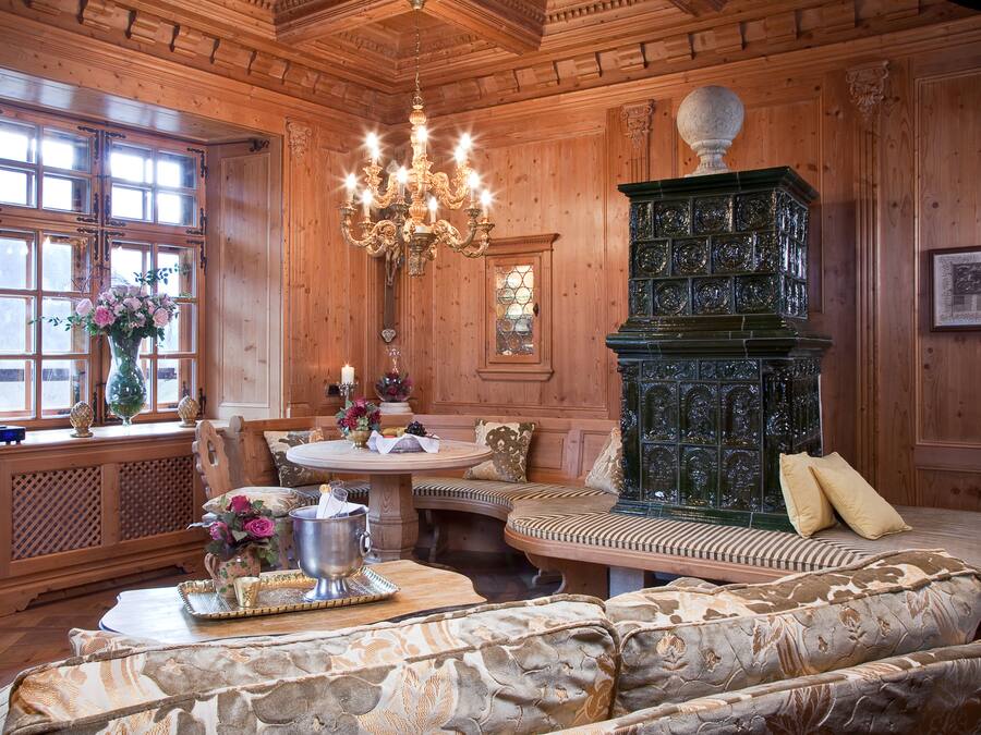 Un interior de madera con un candelabro, una chimenea verde, un sofá y una mesa de comedor.