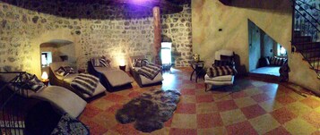 Quarto acolhedor com paredes de pedra, piso xadrez e diversos assentos, incluindo sofás e uma poltrona.