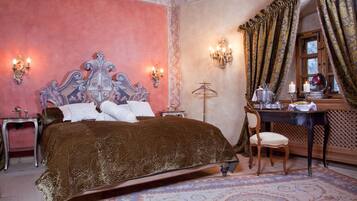A bedroom with a large bed, two bedside tables, a desk with a chair, and a window with curtains.