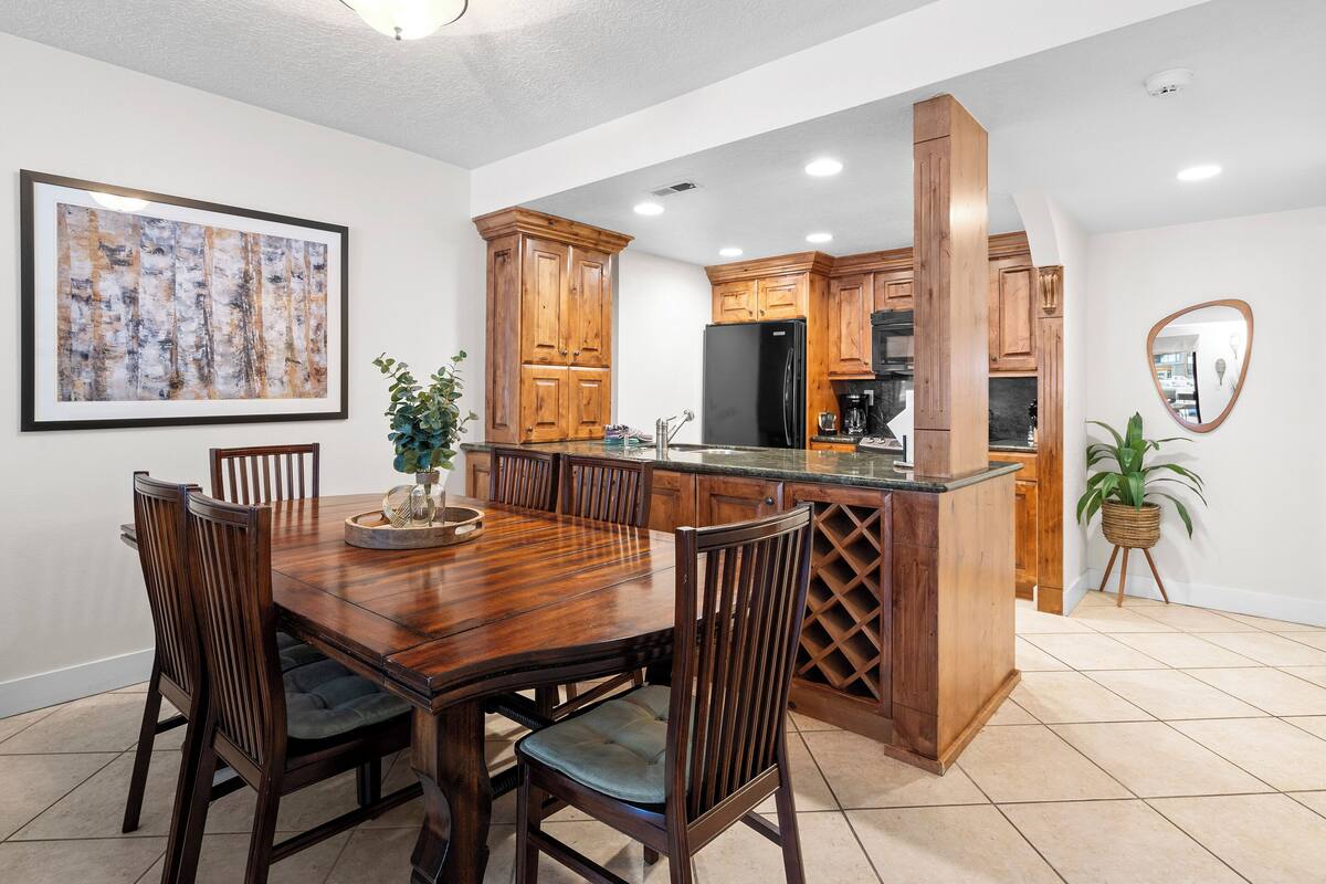 Un comedor con una mesa y sillas de madera, una cocina con armarios de madera, y una obra de arte enmarcada en la pared.