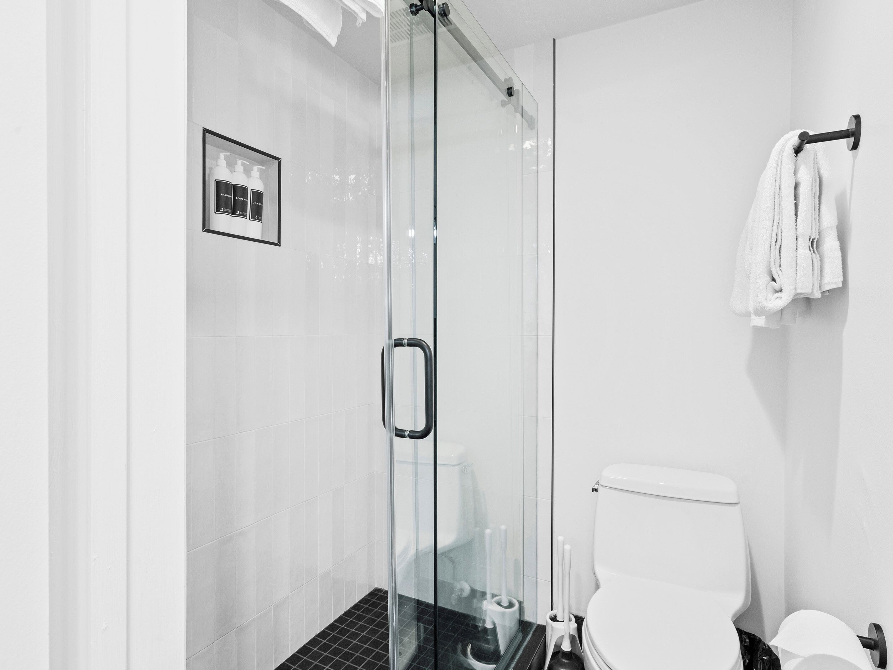 A modern bathroom with a glass shower enclosure, a toilet, and a framed product display.