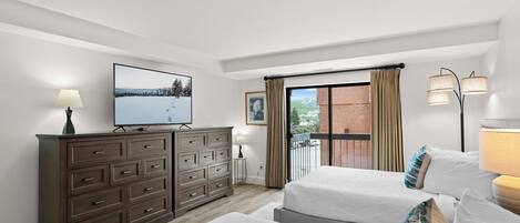 Een slaapkamer met twee bedden, een dressoir, een televisie en een balkon met gordijnen.