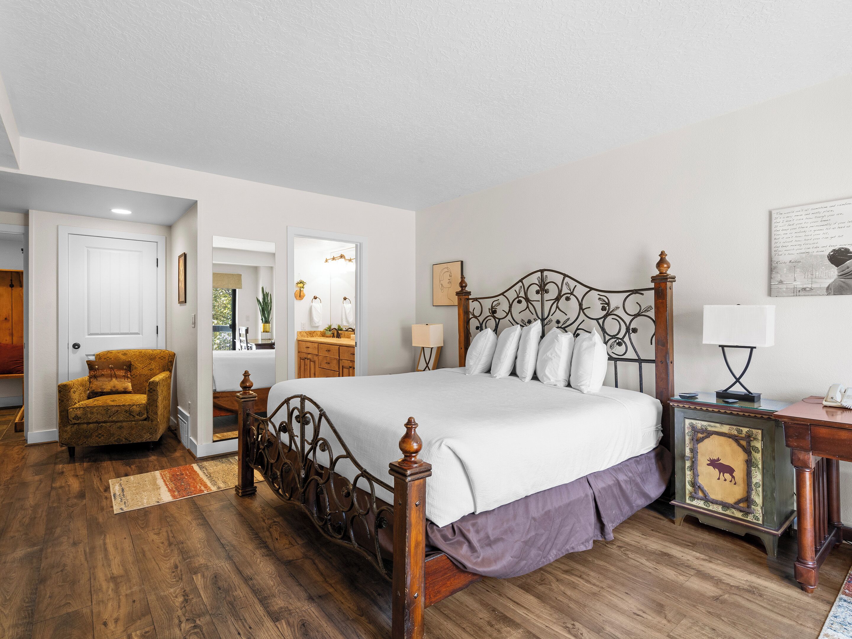 A bedroom with a four-poster bed, a wooden chair, a vanity with a mirror, and a nightstand with a lamp.