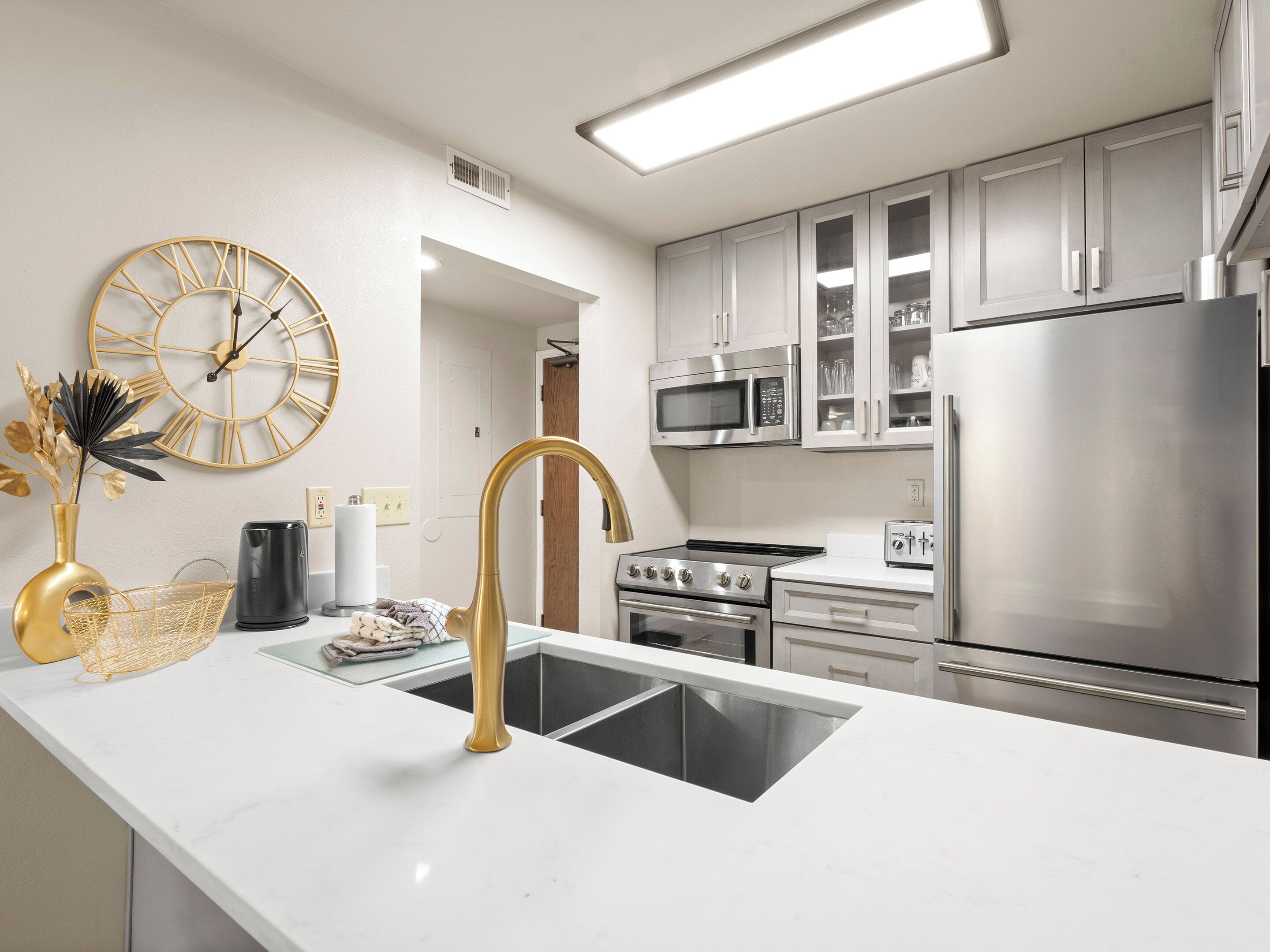 A modern kitchen with white cabinetry, stainless steel appliances, a gold faucet, and a decorative clock.