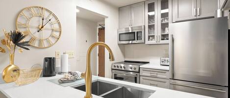 A modern kitchen with white cabinetry, stainless steel appliances, a gold faucet, and a decorative clock.