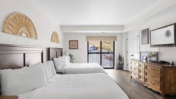 Quarto de hotel com duas camas, cómoda de madeira, televisão e varanda com vista para o exterior.