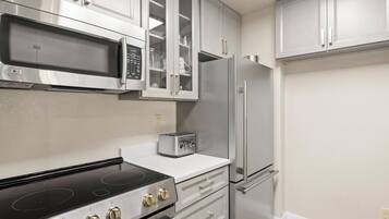 A modern kitchen with stainless steel appliances, including a microwave, oven, and refrigerator, with white cabinetry and a tiled backsplash.