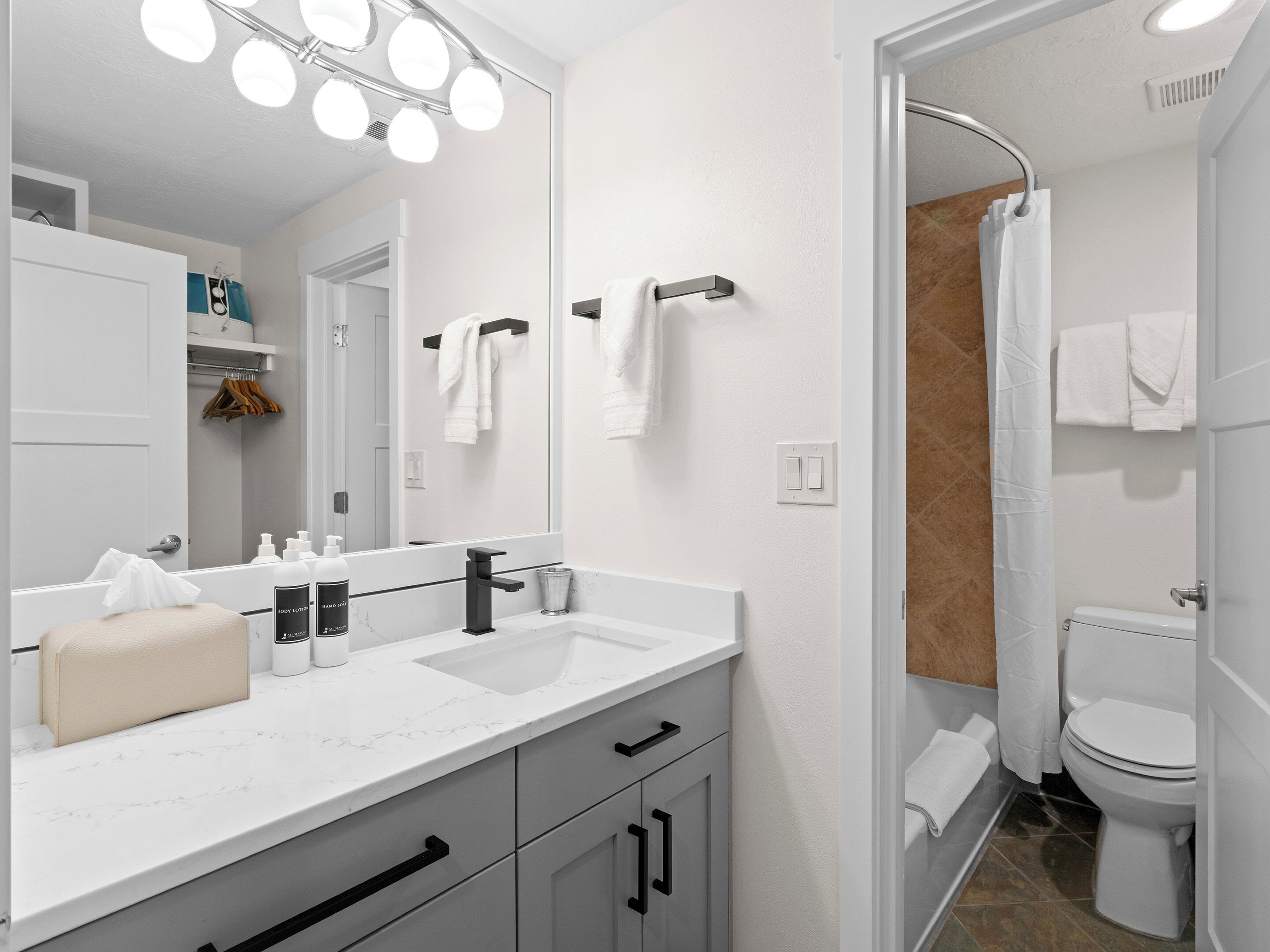 Un baño moderno con tocador doble, un espejo grande con luces, un perchero y una zona de ducha.