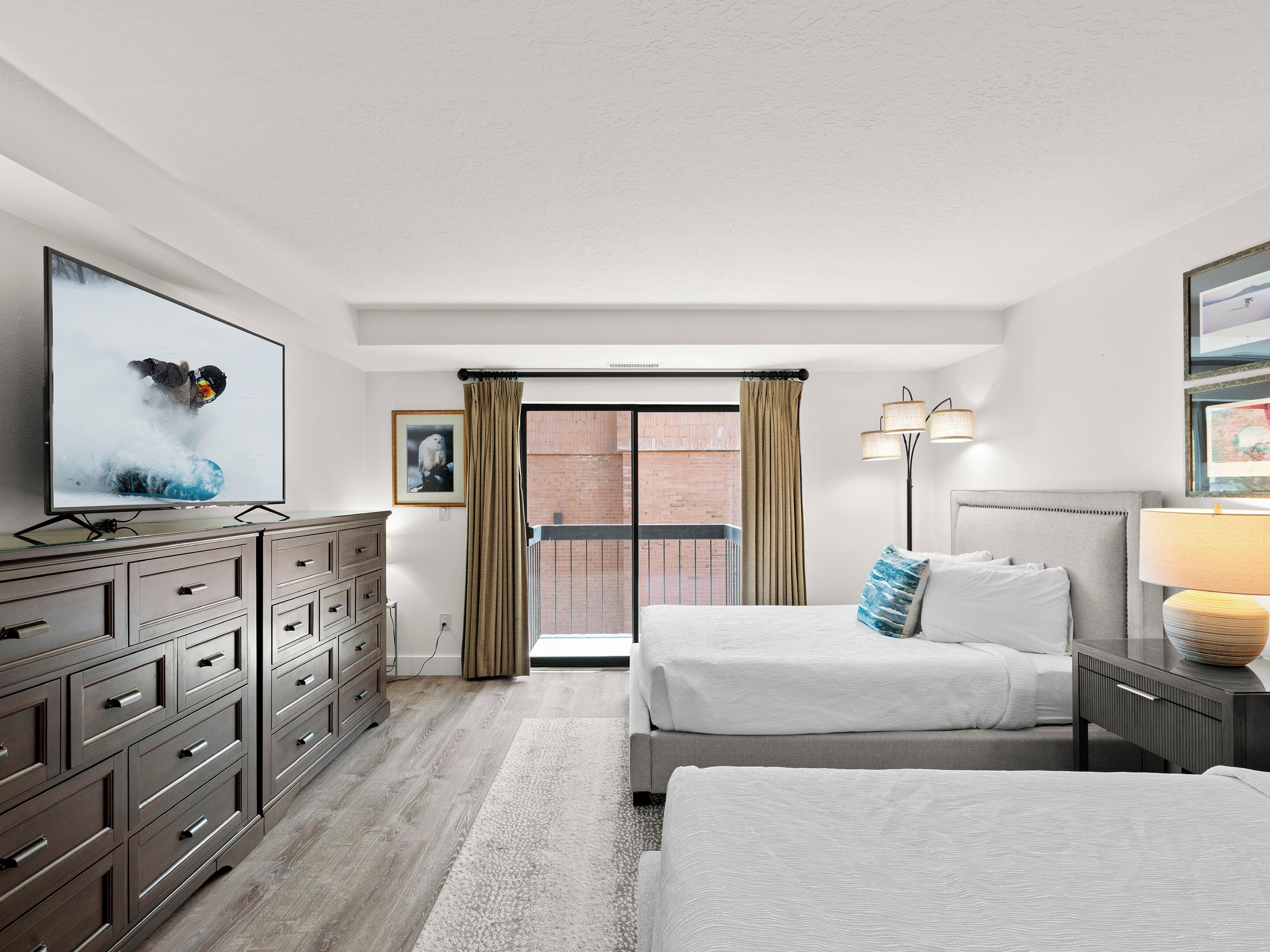 Una habitación de hotel con cama, cómoda, televisor y ventana con cortinas.
